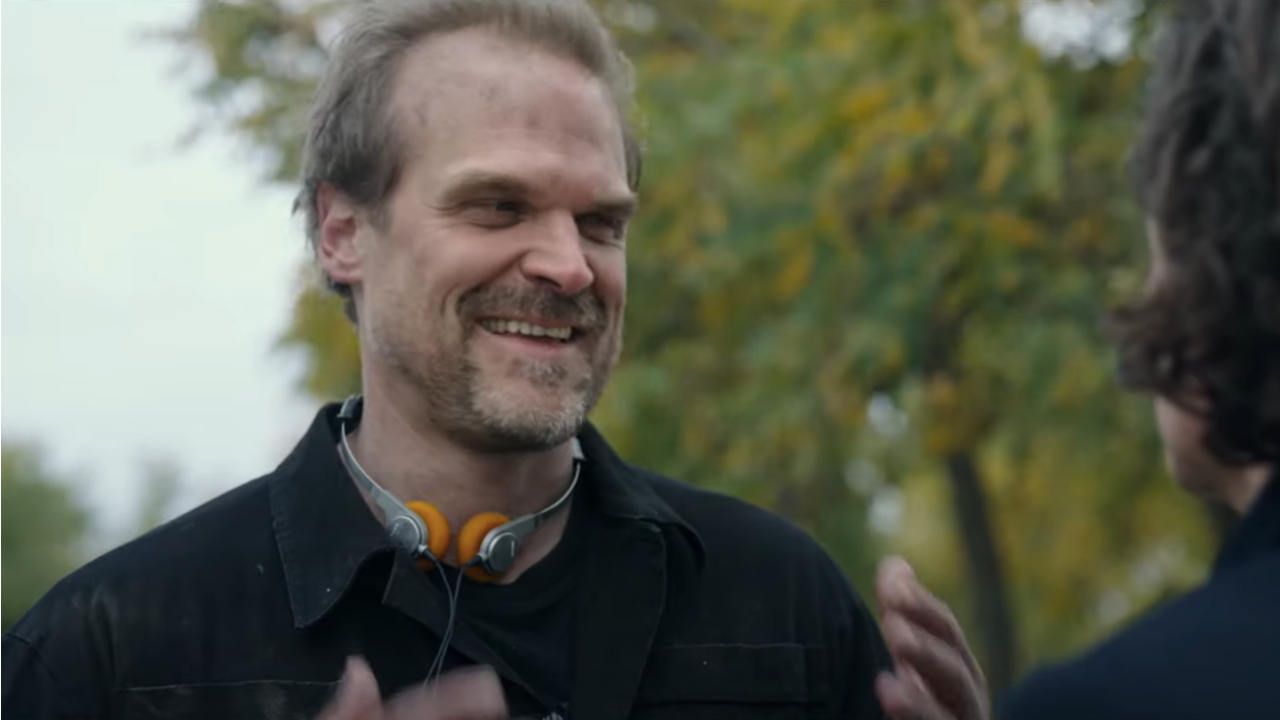 David Harbour lacht ungläubig, während er sich draußen in Gran Turismo unterhält.