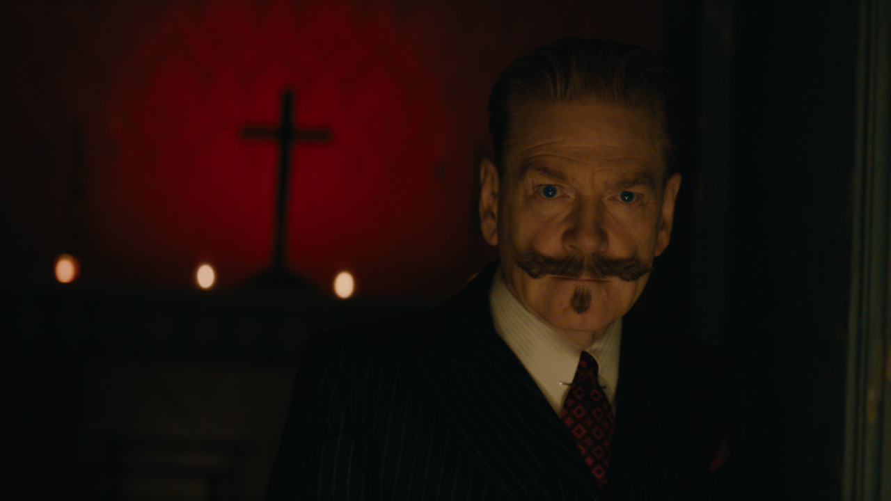 Kenneth Branagh steht in „A Haunting in Venice“ unheimlich vor einem roten Hintergrund mit einem Kreuz.