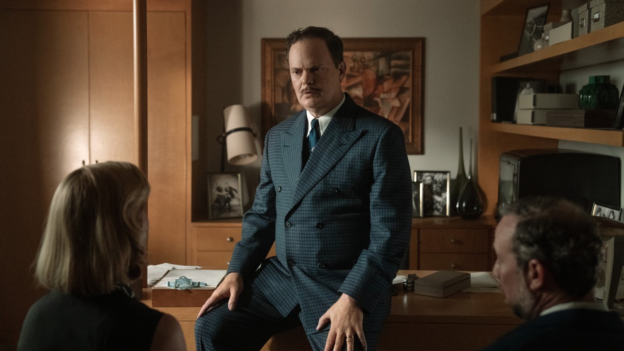 Image de presse de Rainn Wilson dans le rôle de Phil dans Lessons in Chemistry, appuyé contre son bureau et discutant avec Elizabeth et Walter.