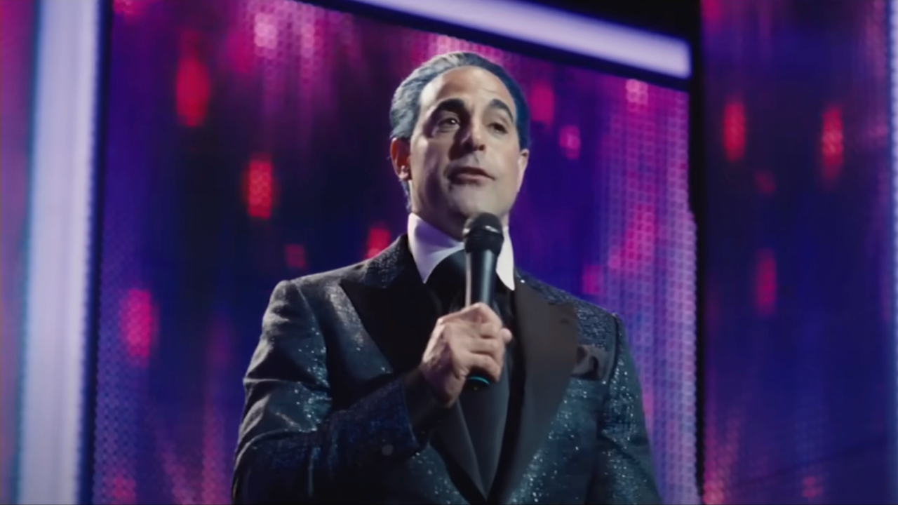 Stanley Tucci präsentiert seine Show in „Die Tribute von Panem“ vor riesigen Bildschirmen.